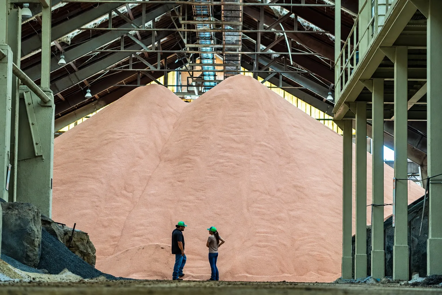 Two Wedgworth’s team members in green hard hats in front of a wall of potash at the Moore Haven ag plant